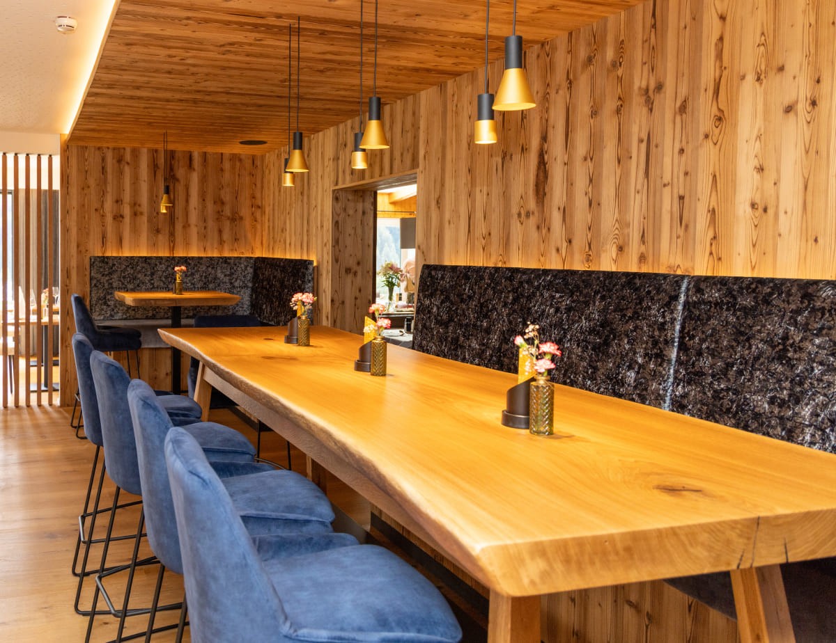 Gem&uuml;tlicher Essbereich mit Holztischen, blauen St&uuml;hlen und warmem Licht