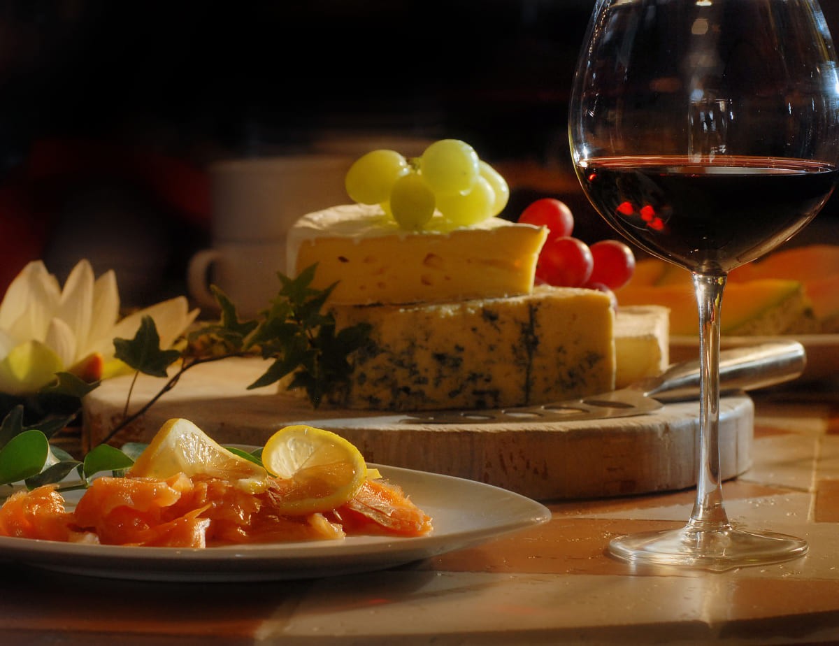 Ein Glas Rotwein, K&auml;sebrett mit Trauben und Teller mit Lachs und Zitrone