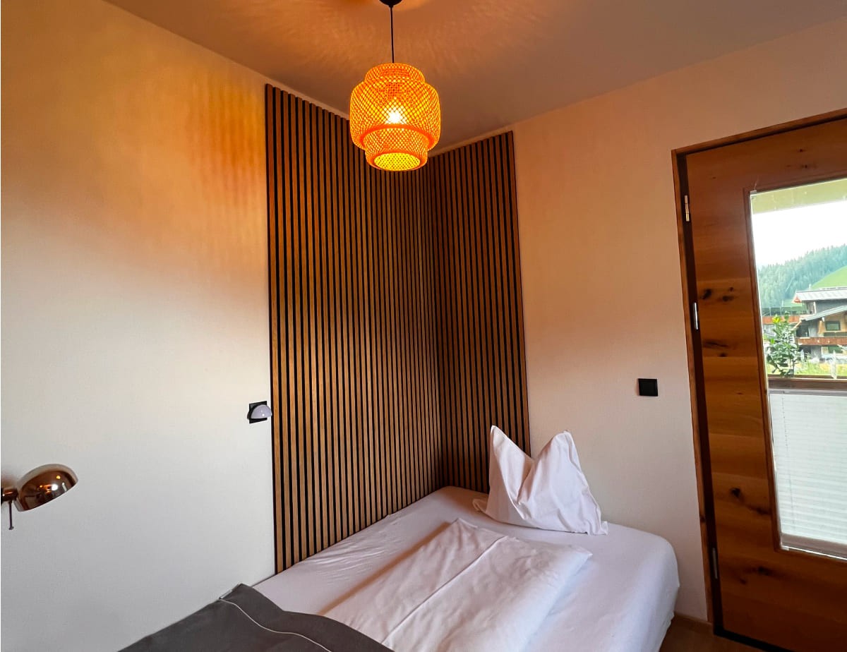 Zimmer mit Einzelbett, Holzverkleidung und leuchtender H&auml;ngelampe