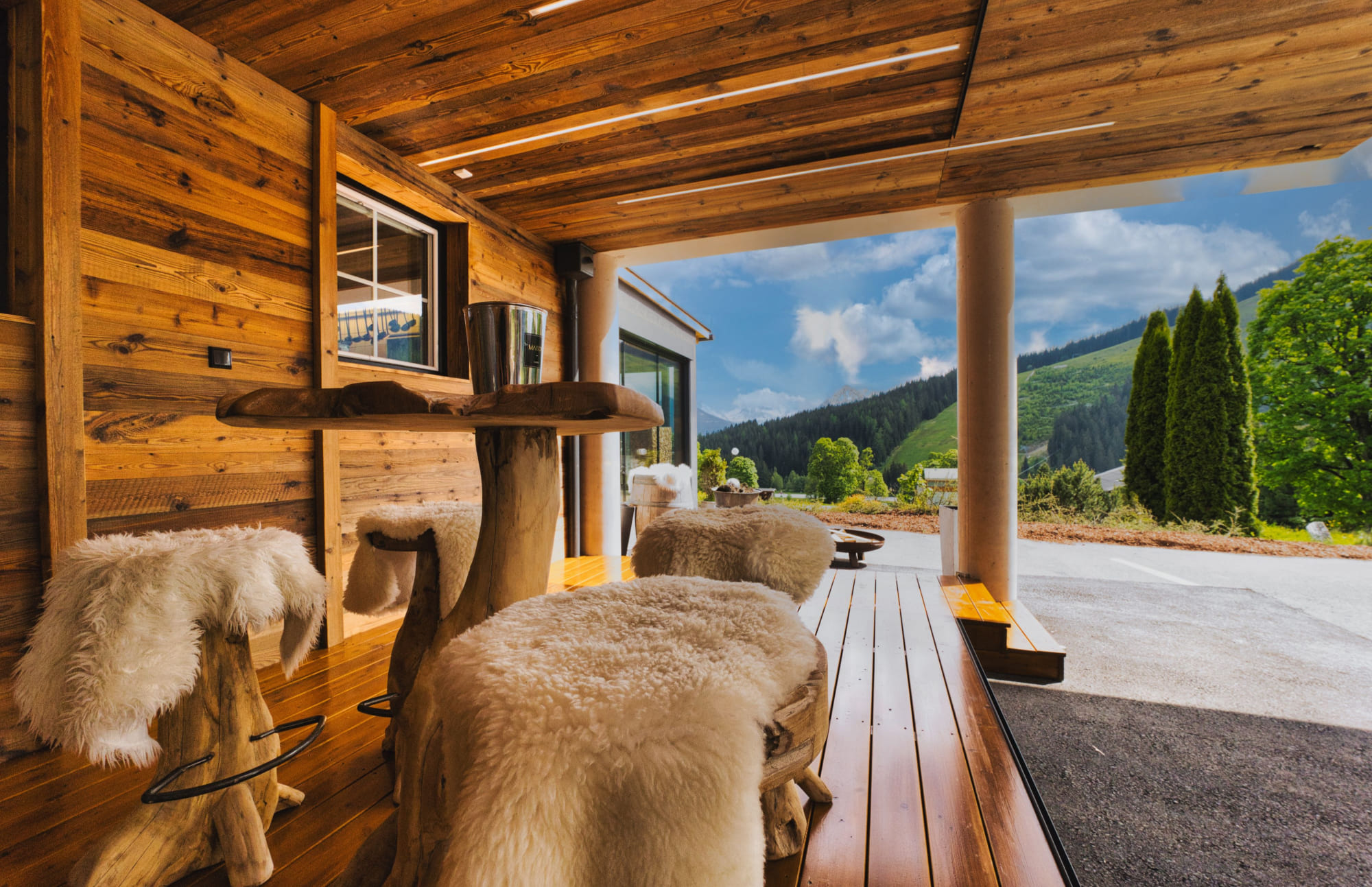 Holzveranda mit Lammfellen und Blick auf grüne Hügel unter blauem Himmel