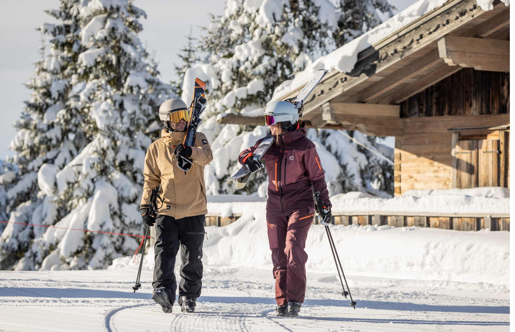 Zwei Skifahrer tragen ihre Skier über den Schultern und gehen durch schneebedeckte Landschaft im Skiurlaub in der Region Schladming-Dachstein