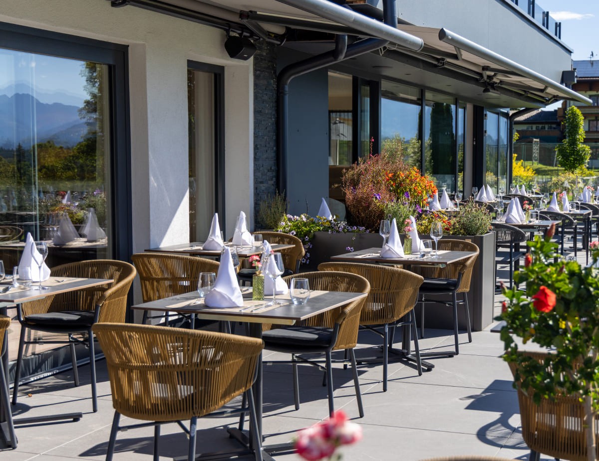 Au&szlig;enbereich eines Restaurants mit gedeckten Tischen und Blumen im Sonnenschein