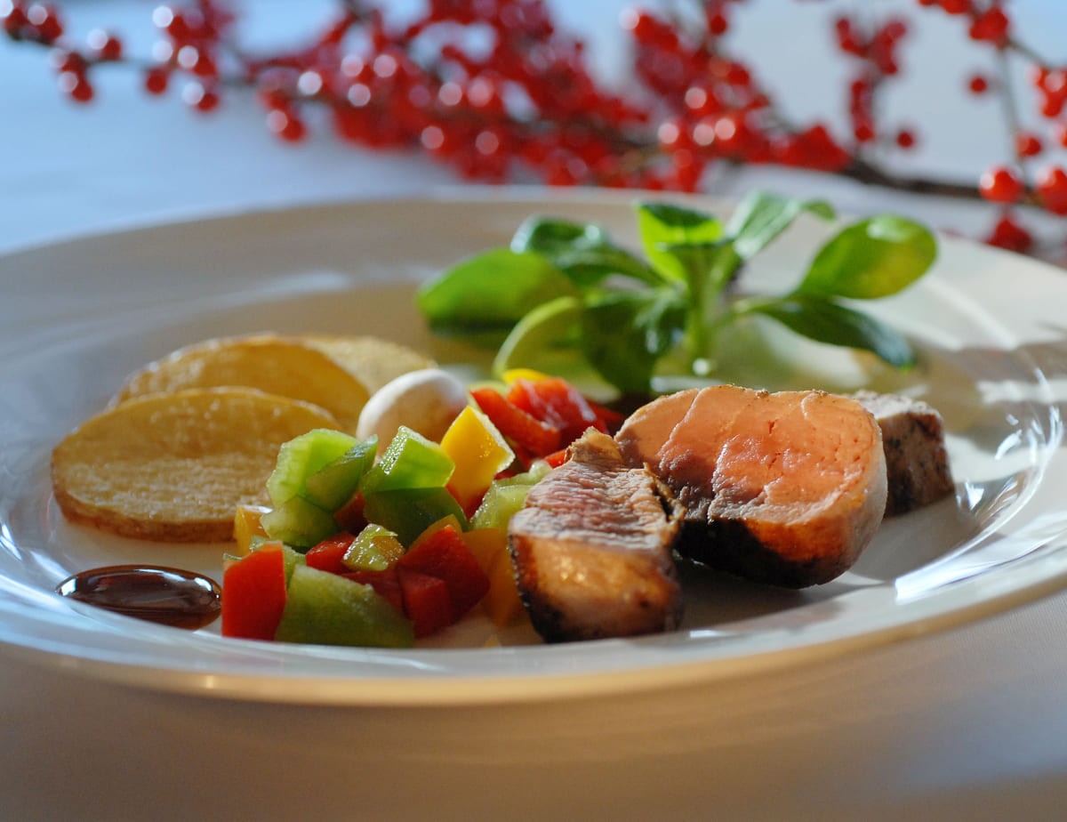 Gourmet-Teller mit Fleisch, Gem&uuml;se, Chips und Salat, im Hintergrund rote Beeren