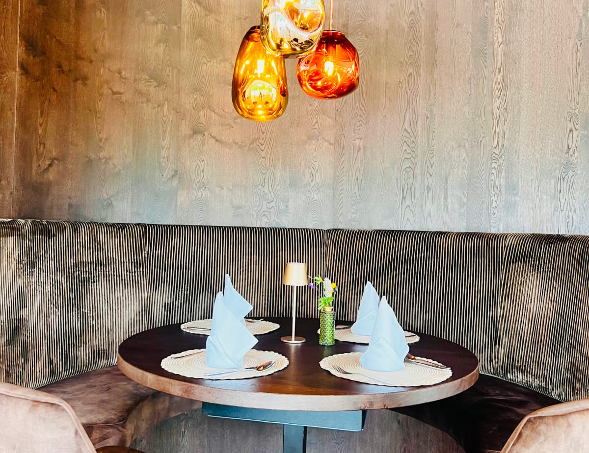 Ein runder Tisch mit vier Gedecken und gefalteten Servietten in gem&uuml;tlichen Restaurant im Landhaus Ramsau