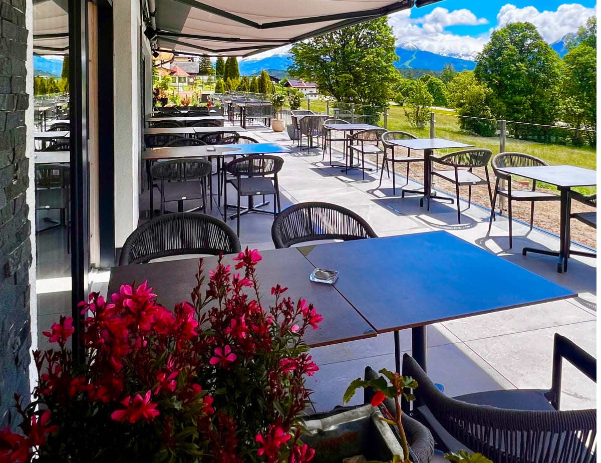 Sonnige Terrasse mit Tischen, St&uuml;hlen und Blumen, mit Bergblick im Hintergrund