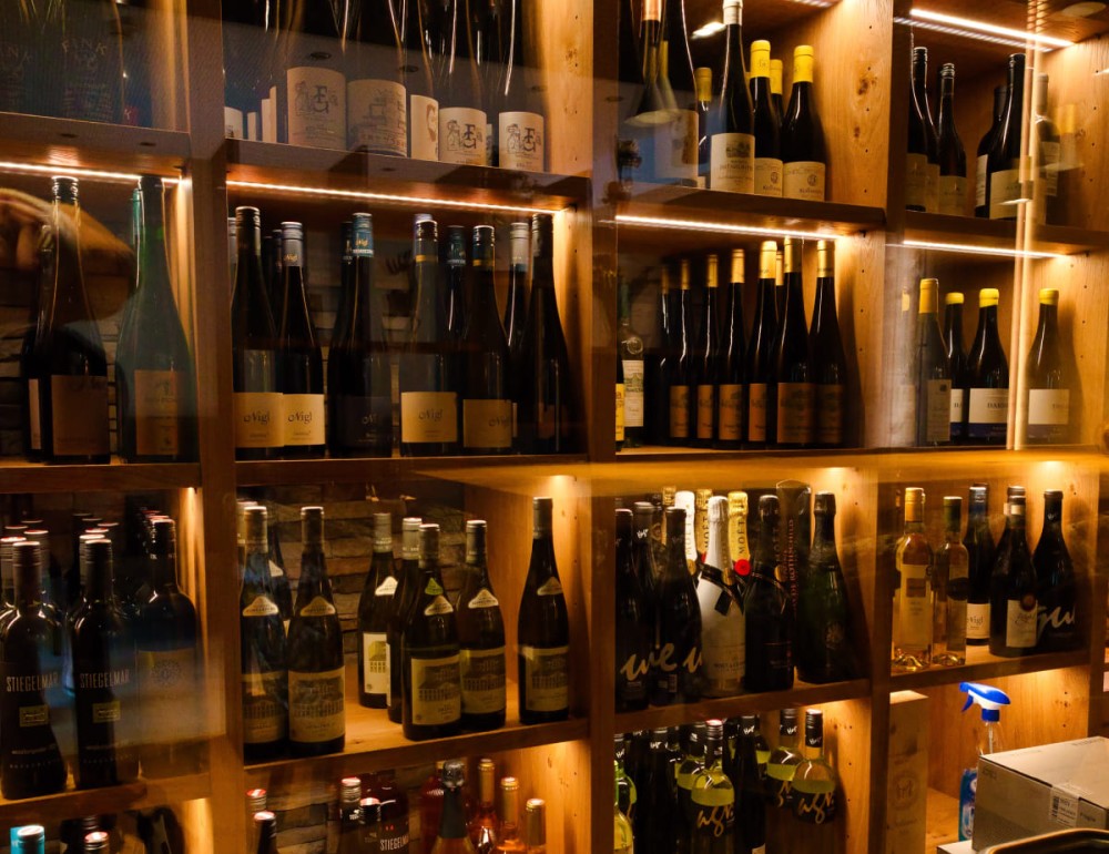 Ein Regal mit vielen Weinflaschen, beleuchtet und geordnet im Hotel Landhaus Ramsau mit Weinbar
