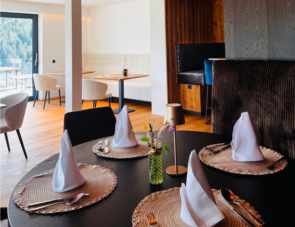 Elegantes Restaurant im Landhaus Ramsau mit gedecktem Tisch und Blick auf Wald durch gro&szlig;e Fenster
