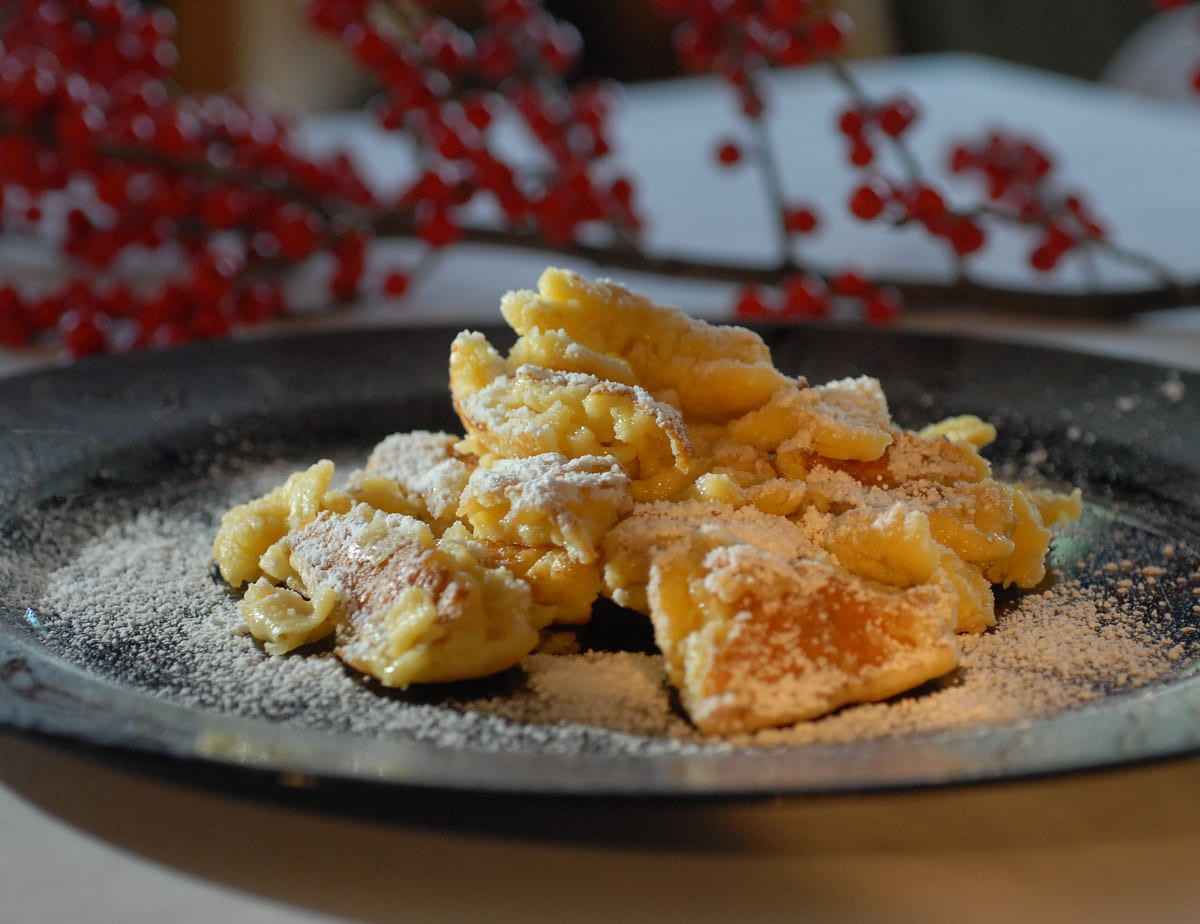 Kaiserschmarrn auf einem Teller mit Puderzucker best&auml;ubt, im Hintergrund rote Beeren
