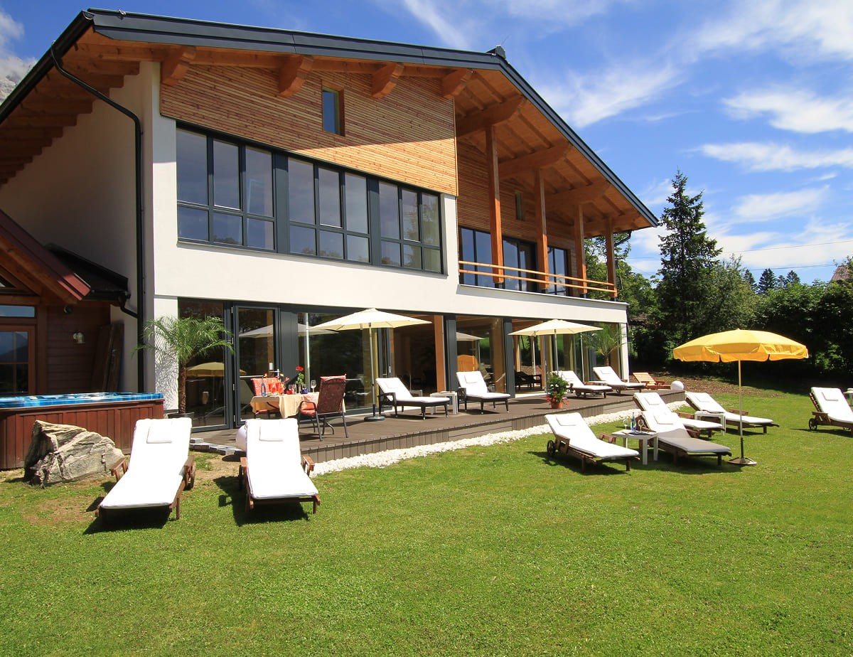 Modernes Haus mit gro&szlig;er Terrasse und Sonnenliegen im Garten unter blauem Himmel