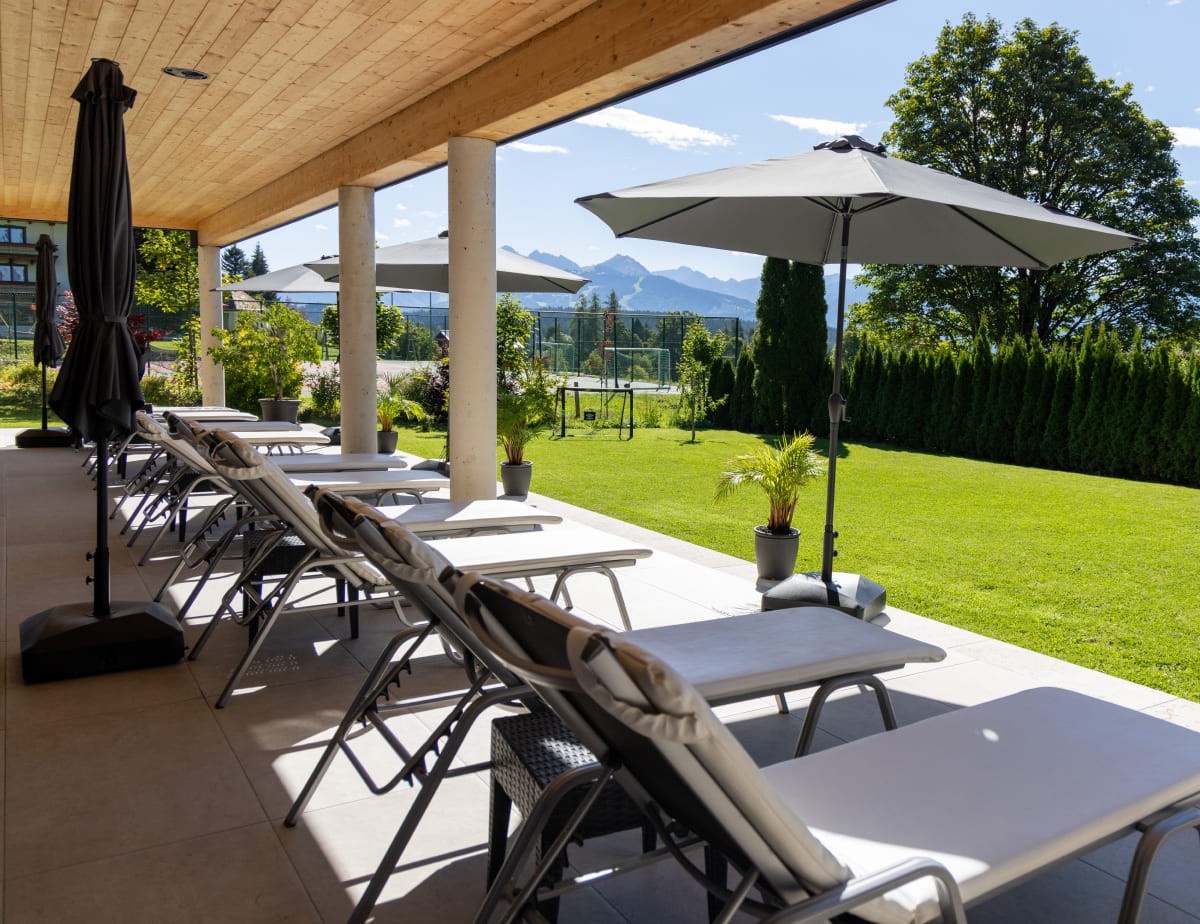 Eine Terrasse mit Liegest&uuml;hlen, Sonnenschirmen und Blick auf einen gr&uuml;nen Garten