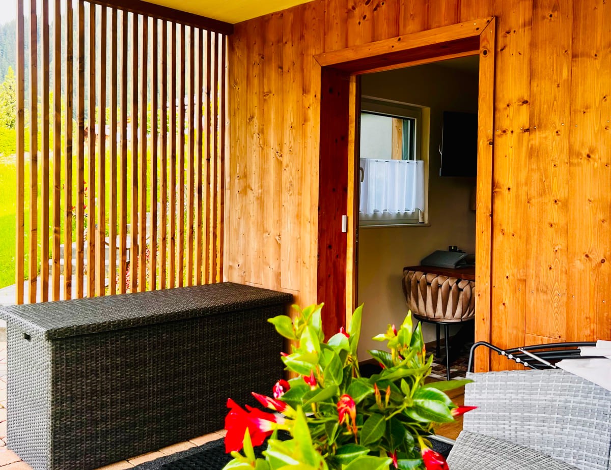 Holzveranda mit Pflanzen und Blick ins Innere eines Hauses durch eine offene T&uuml;r
