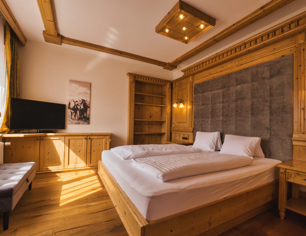 Holzvert&auml;feltes Schlafzimmer mit Doppelbett, TV und Bild einer Kuhherde an der Wand
