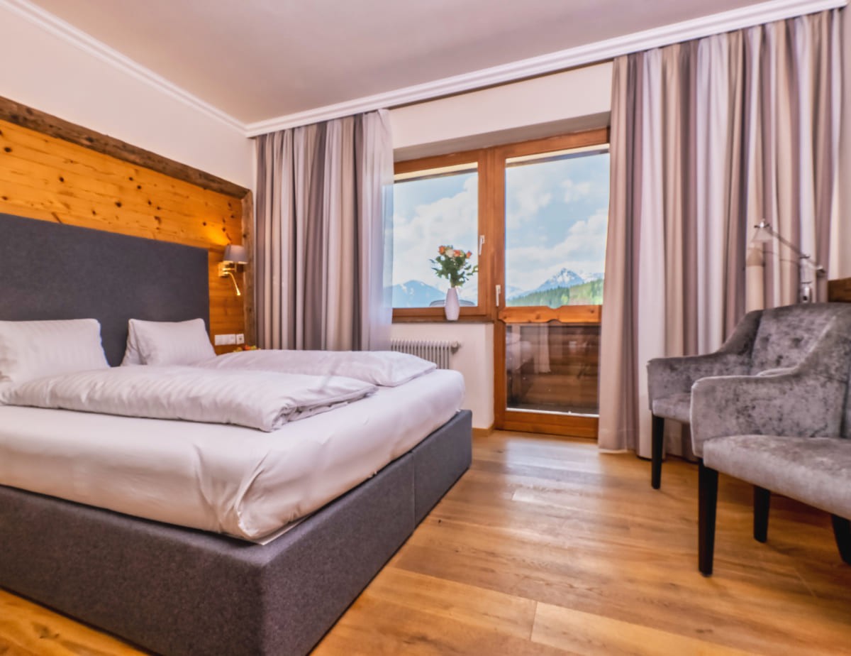 Gem&uuml;tliches Hotelzimmer mit gro&szlig;em Bett und Bergblick durch das Fenster