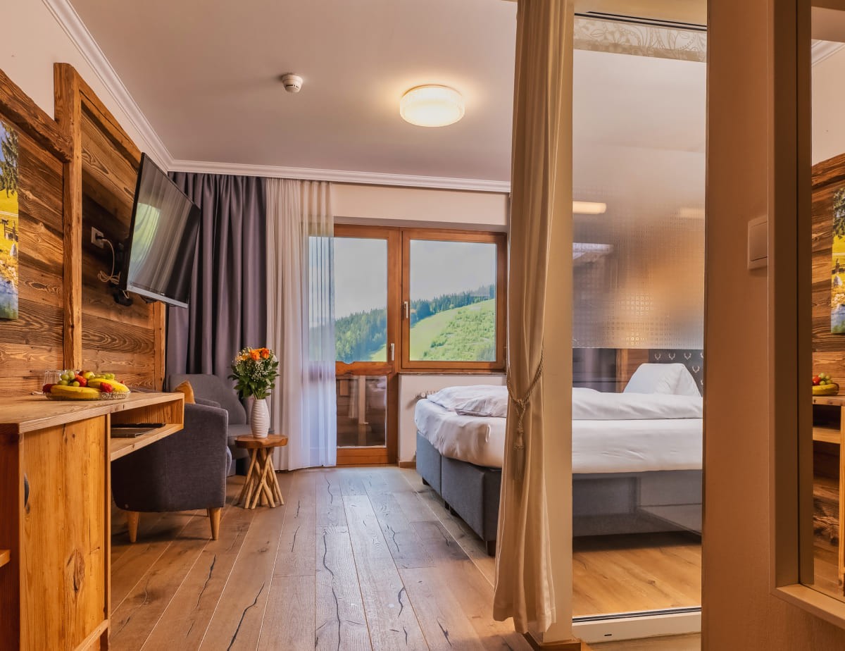 Gem&uuml;tliches Hotelzimmer mit Holzm&ouml;beln und Balkon mit Ausblick auf gr&uuml;ne H&uuml;gel