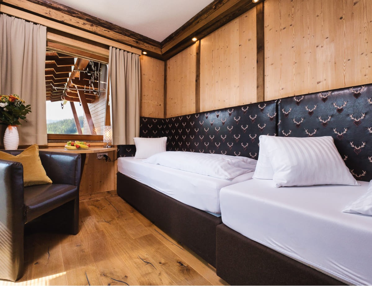 Gem&uuml;tliches Familienzimmer mit Holzw&auml;nden, Doppelbett und Blick aus dem Fenster