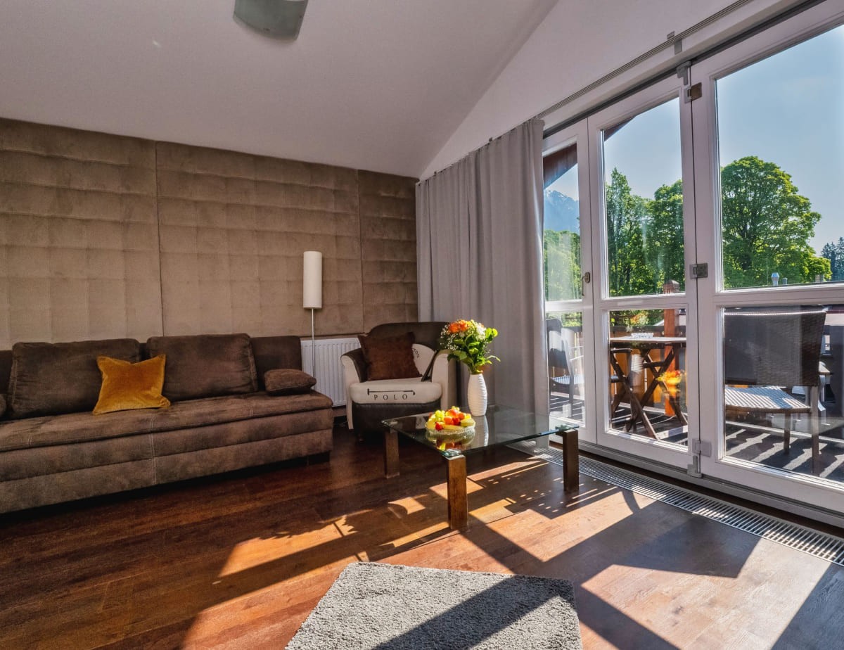 Gem&uuml;tliches Wohnzimmer mit gro&szlig;en Fenstern und braunem Sofa, Blick auf Terrasse