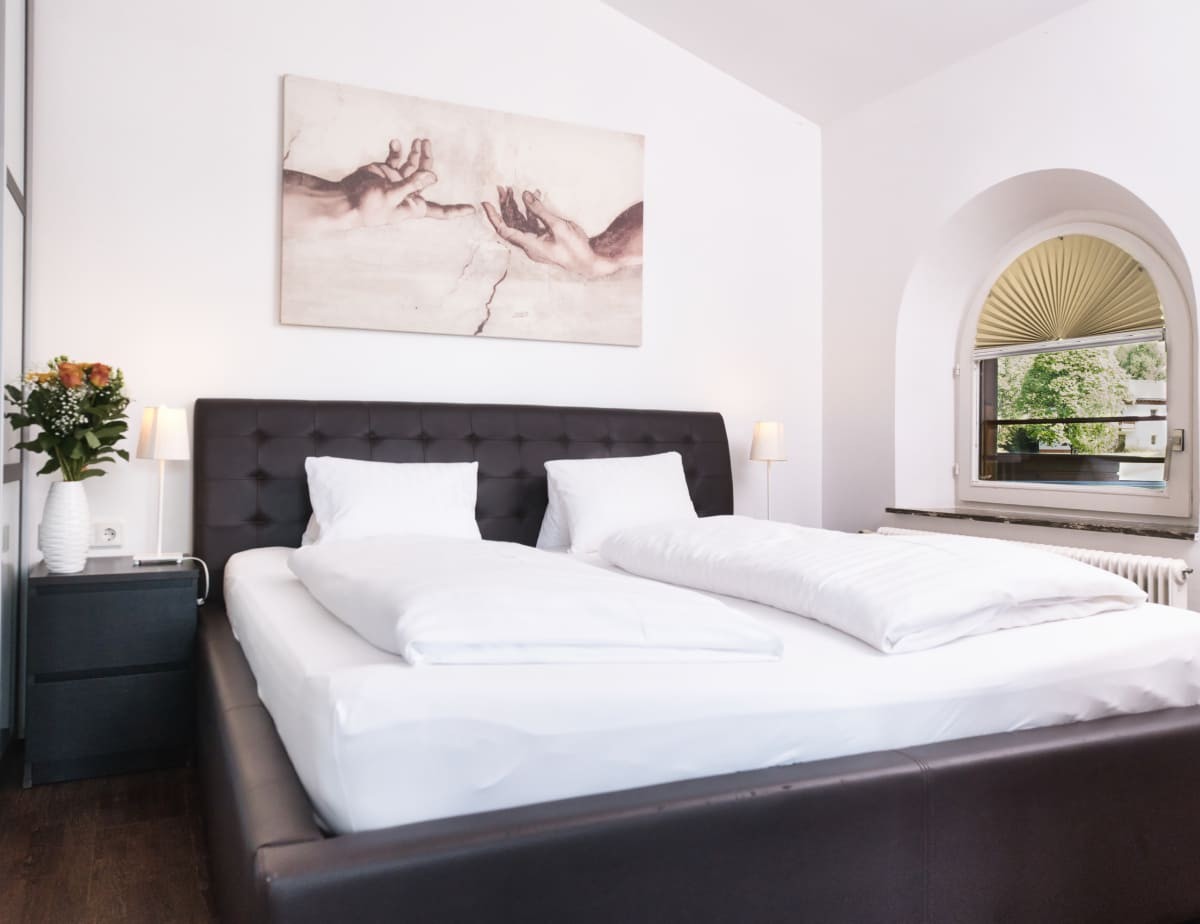 Modernes Schlafzimmer mit gro&szlig;em Bett, zwei Nachttischen und einem Fenster mit Blick ins Gr&uuml;ne