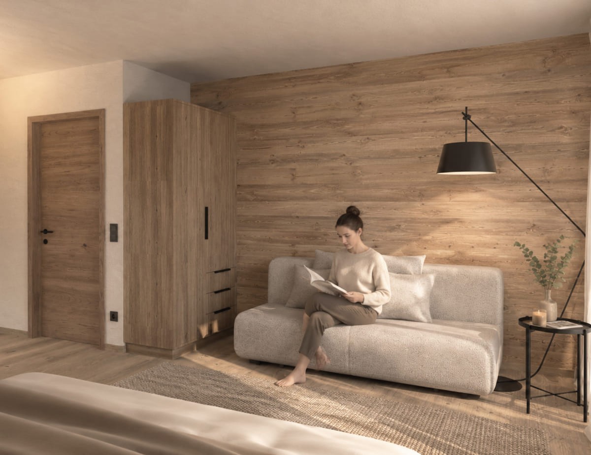 Visualisierung vom neuen Zimmer im Hotel Landhaus, Eine Person liest auf einem Sofa in einem gem&uuml;tlich eingerichteten Zimmer